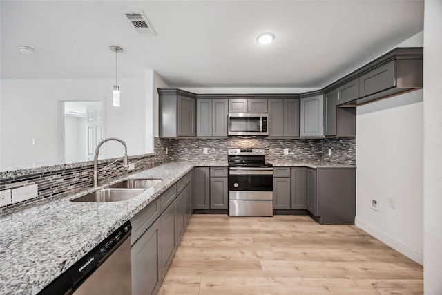 kitchen featuring pendant lighting, sink, stainless steel appliances, light stone counters, and light wood-type flooring
