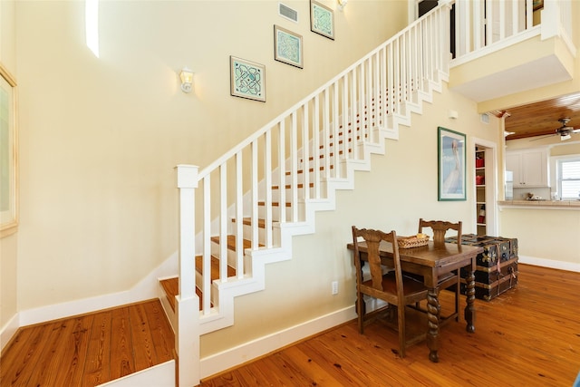 stairs featuring ceiling fan, a high ceiling, and wood-type flooring