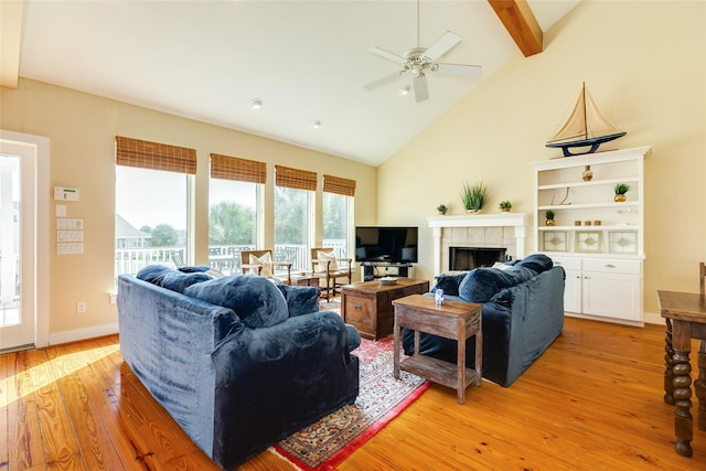 living room featuring light wood-type flooring, beamed ceiling, ceiling fan, a fireplace, and high vaulted ceiling