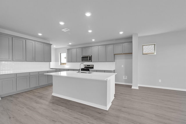 kitchen featuring a sink, appliances with stainless steel finishes, a center island with sink, and gray cabinetry