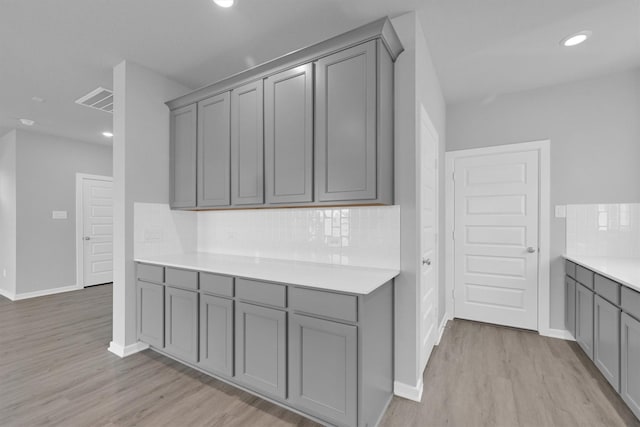 kitchen featuring backsplash, baseboards, light countertops, gray cabinets, and light wood-style flooring