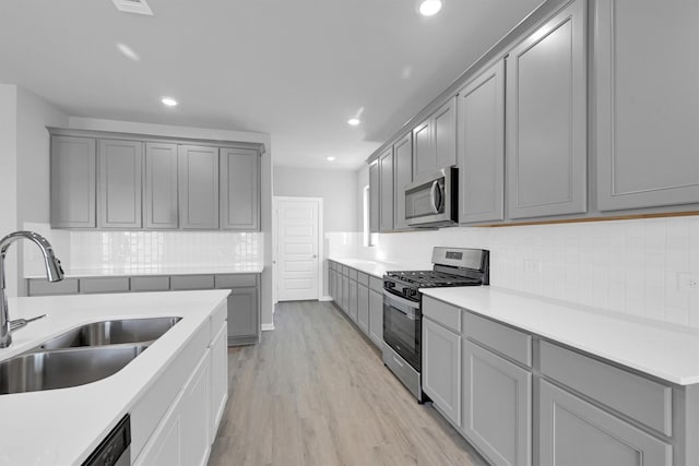 kitchen featuring a sink, stainless steel appliances, gray cabinetry, and light wood-style flooring