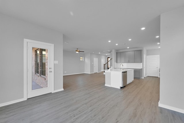 kitchen with light wood finished floors, open floor plan, gray cabinets, stainless steel dishwasher, and a sink