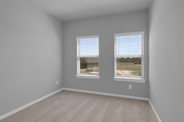 spare room featuring light colored carpet and baseboards