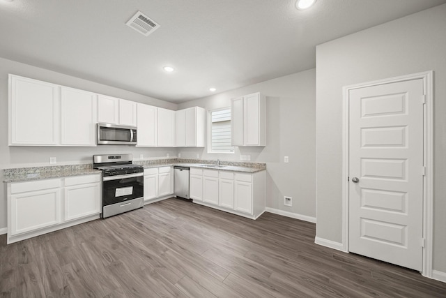 kitchen with stainless steel appliances, white cabinetry, a sink, and visible vents