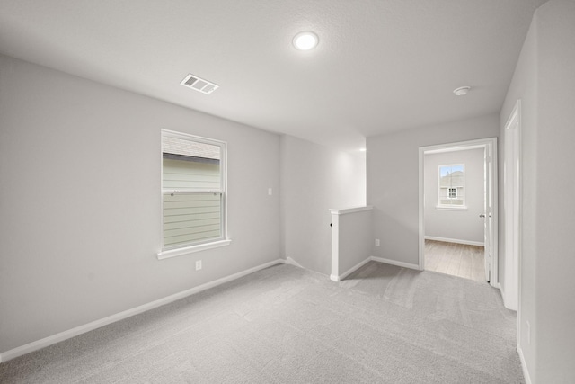 spare room with light colored carpet, visible vents, and baseboards