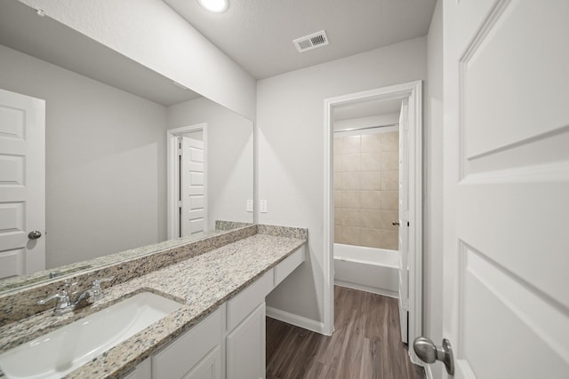 full bath featuring wood finished floors, vanity, baseboards, visible vents, and shower / bathing tub combination