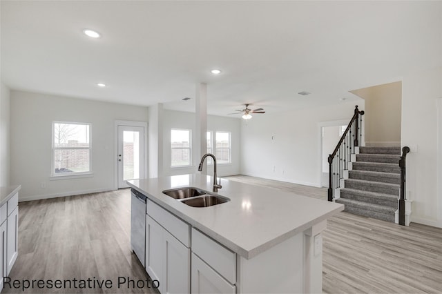 kitchen featuring sink, white cabinetry, light wood-type flooring, stainless steel dishwasher, and a kitchen island with sink