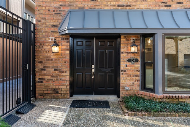 view of exterior entry featuring brick siding and a standing seam roof