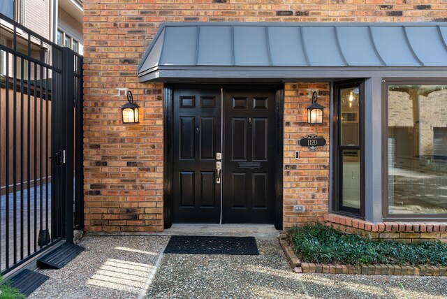 view of exterior entry featuring brick siding and a standing seam roof