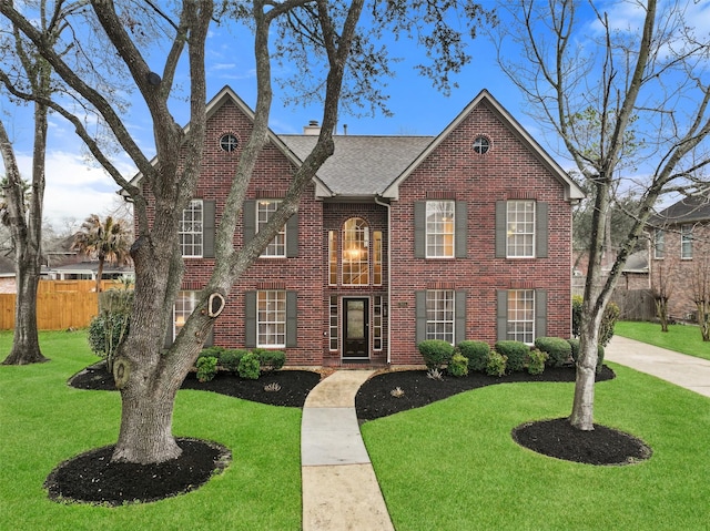 view of front of house featuring brick siding, a chimney, a shingled roof, fence, and a front lawn