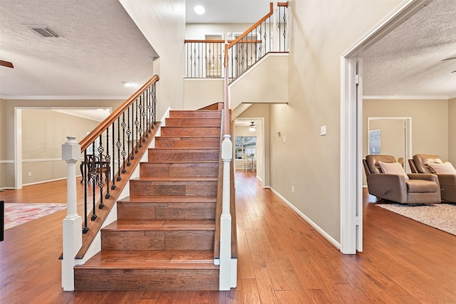 stairway with ornamental molding, ceiling fan, a textured ceiling, wood finished floors, and baseboards