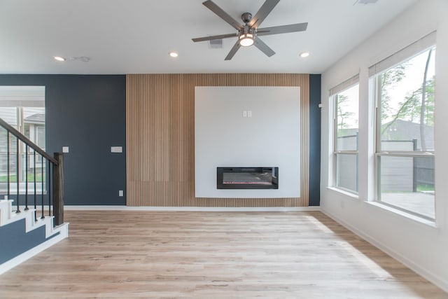 unfurnished living room with light wood-style floors, stairway, a glass covered fireplace, and baseboards