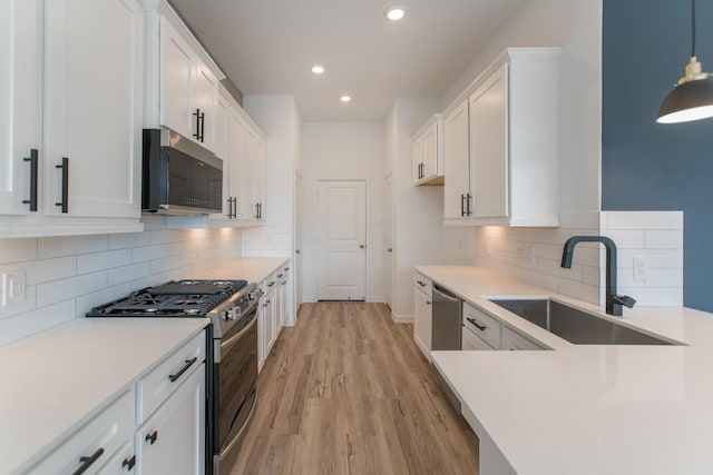 kitchen with stainless steel appliances, white cabinets, a sink, and light wood-style flooring