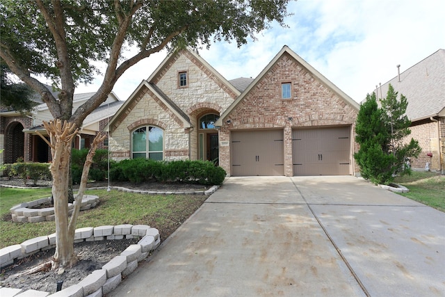 french country inspired facade featuring an attached garage, concrete driveway, and brick siding