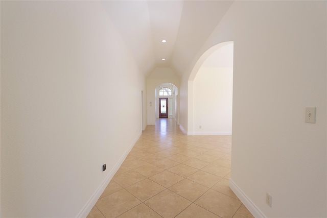 corridor featuring arched walkways, light tile patterned floors, recessed lighting, lofted ceiling, and baseboards