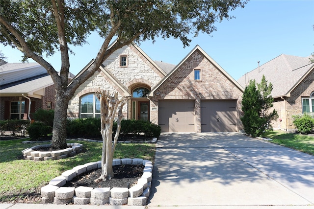 french country inspired facade with a garage, concrete driveway, brick siding, and stone siding