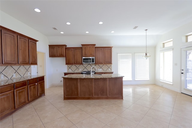 kitchen with an island with sink, lofted ceiling, stainless steel microwave, hanging light fixtures, and light stone countertops