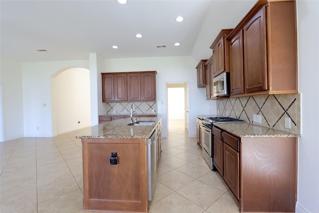 kitchen featuring stainless steel appliances, light stone counters, a sink, and a center island with sink