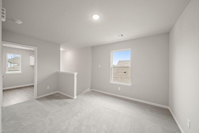 unfurnished room featuring light carpet, a wealth of natural light, visible vents, and baseboards