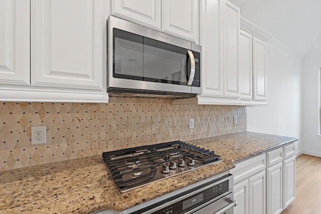 kitchen featuring white cabinetry, crown molding, appliances with stainless steel finishes, light stone countertops, and decorative backsplash