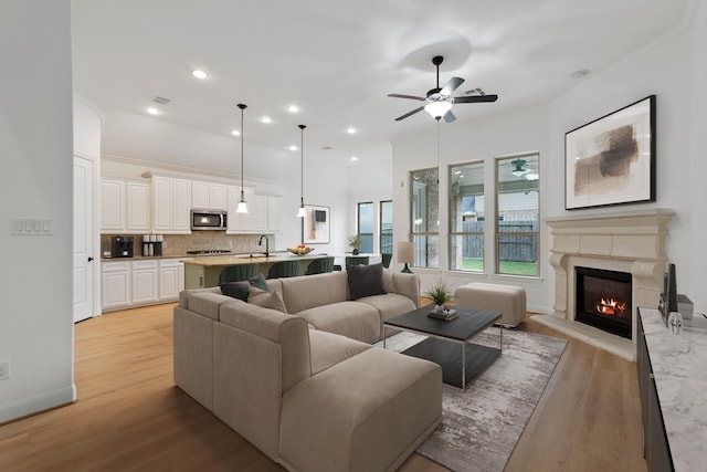 living room with ceiling fan, sink, a fireplace, and light hardwood / wood-style floors