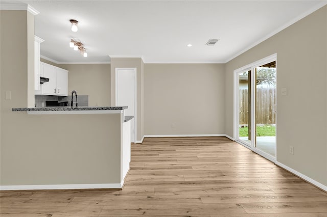 kitchen with white cabinetry, ornamental molding, dark stone counters, and a healthy amount of sunlight