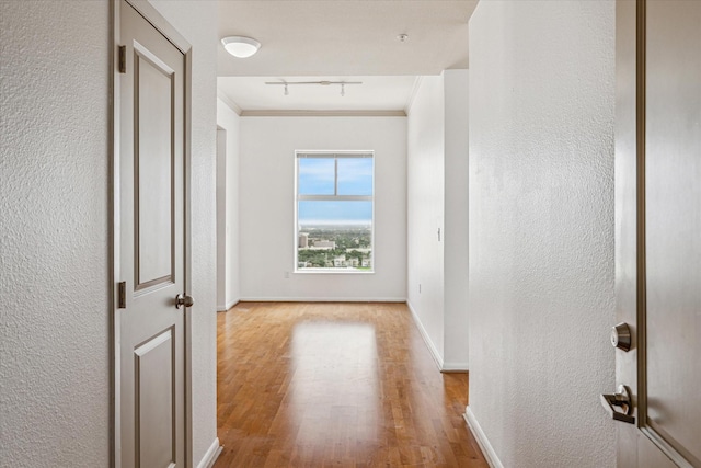 hallway with baseboards, a textured wall, ornamental molding, rail lighting, and light wood-type flooring