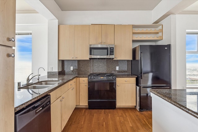 kitchen featuring dark stone counters, wood finished floors, light brown cabinetry, black appliances, and a sink