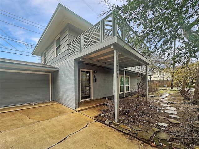 view of front facade featuring driveway, brick siding, and a balcony