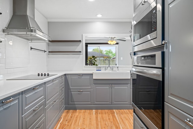 kitchen with wall chimney exhaust hood, sink, appliances with stainless steel finishes, gray cabinets, and backsplash