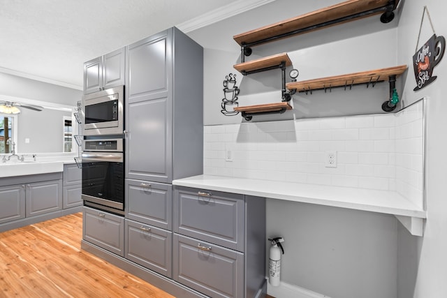 kitchen with gray cabinets, crown molding, appliances with stainless steel finishes, and backsplash