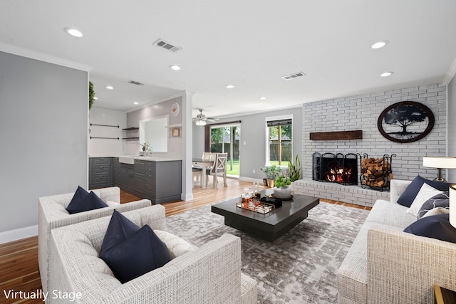 living room featuring a fireplace, crown molding, wood-type flooring, and ceiling fan