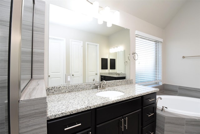 bathroom with vanity, lofted ceiling, and a relaxing tiled tub