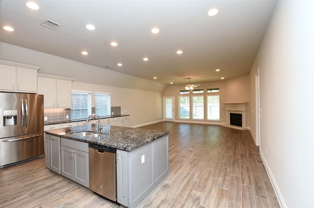 kitchen featuring sink, white cabinetry, stainless steel appliances, an island with sink, and dark stone counters