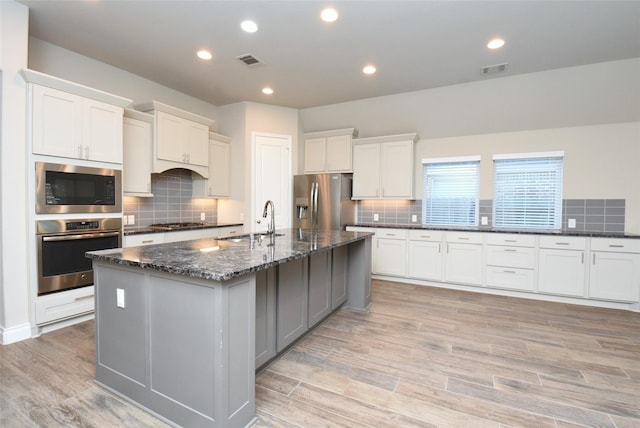 kitchen with a kitchen island with sink, sink, white cabinets, and appliances with stainless steel finishes