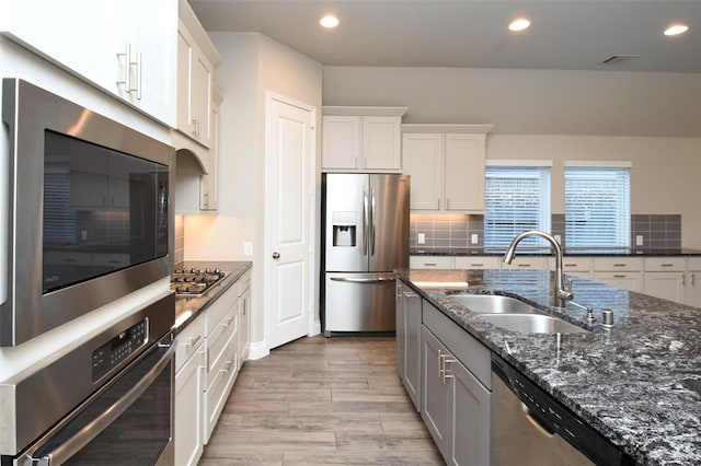 kitchen featuring sink, appliances with stainless steel finishes, white cabinetry, tasteful backsplash, and dark stone counters