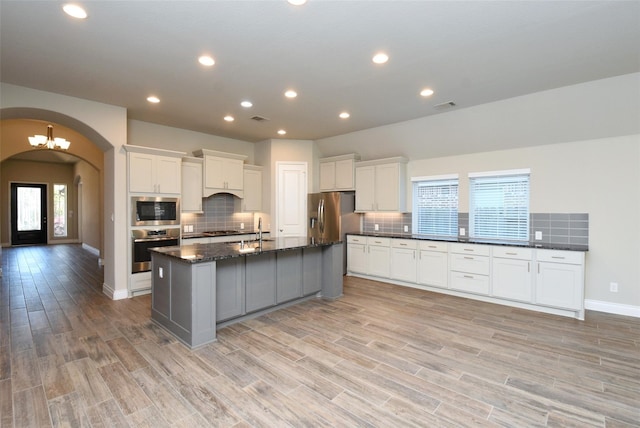 kitchen with dark stone countertops, stainless steel appliances, a center island with sink, and white cabinets