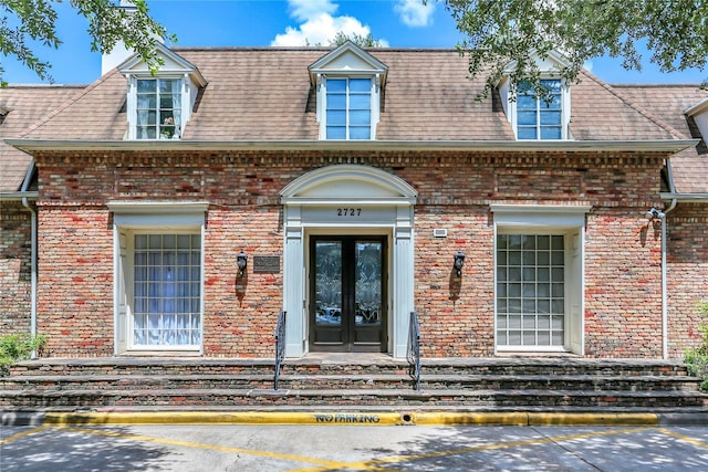 entrance to property featuring french doors, brick siding, and roof with shingles