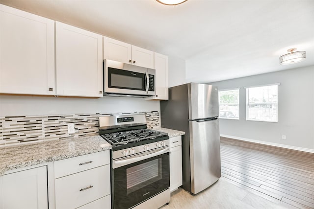 kitchen with appliances with stainless steel finishes, white cabinetry, backsplash, light stone counters, and light hardwood / wood-style flooring