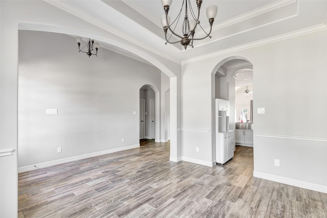 spare room featuring a raised ceiling, ornamental molding, light wood-type flooring, and an inviting chandelier