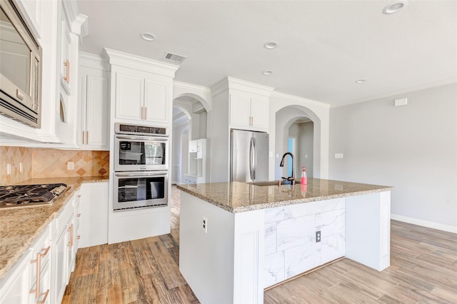 kitchen with sink, appliances with stainless steel finishes, light stone countertops, a kitchen island with sink, and white cabinets