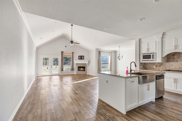 kitchen with stone counters, appliances with stainless steel finishes, white cabinetry, sink, and a center island with sink