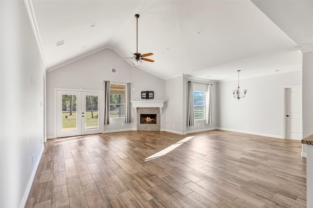 unfurnished living room with vaulted ceiling, ceiling fan with notable chandelier, light hardwood / wood-style floors, and french doors