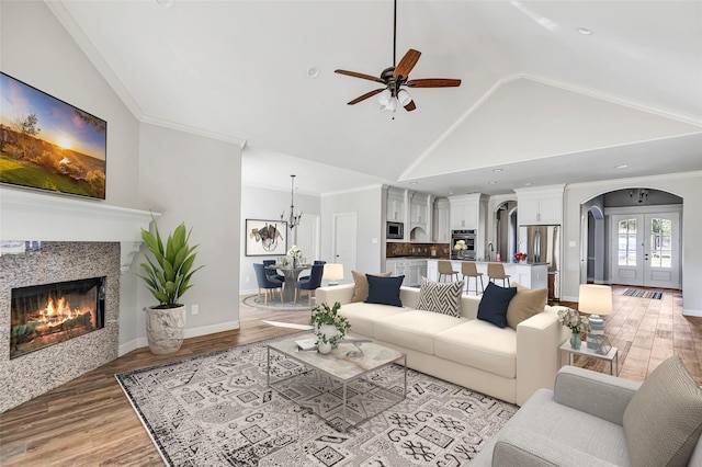 living room with high vaulted ceiling, a fireplace, ornamental molding, light wood-type flooring, and french doors