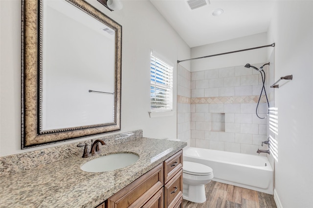 full bathroom with wood-type flooring, tiled shower / bath, vanity, and toilet