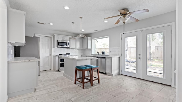 kitchen with appliances with stainless steel finishes, decorative light fixtures, a kitchen breakfast bar, a center island, and french doors