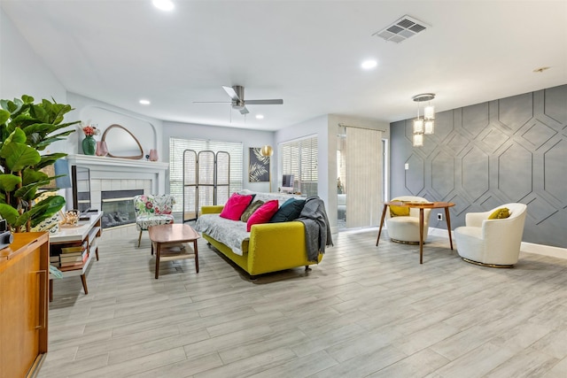 living room featuring ceiling fan, light hardwood / wood-style flooring, and a tiled fireplace