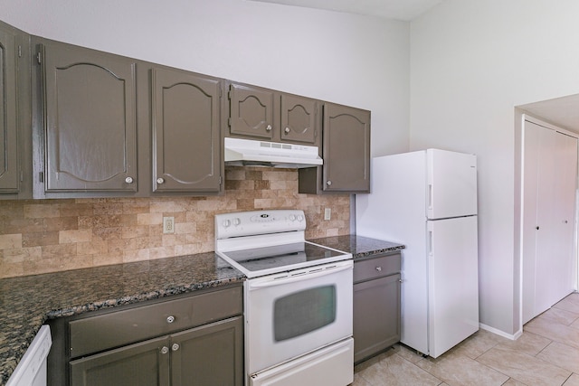 kitchen with light tile patterned flooring, dark stone counters, white appliances, and decorative backsplash