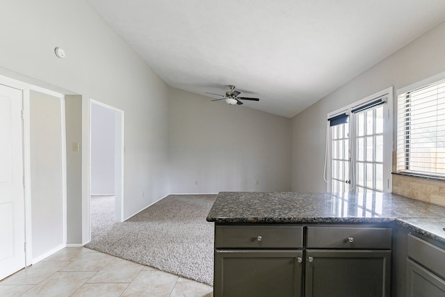 kitchen featuring vaulted ceiling, light colored carpet, dark stone counters, and ceiling fan